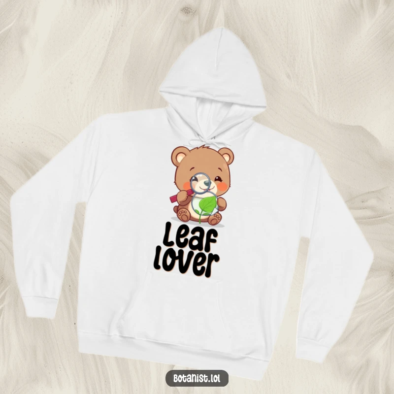 A cheerful, funny bear cub using a magnifying glass to inspect a tiny, sentient leaf, printed on a soft hoodie.