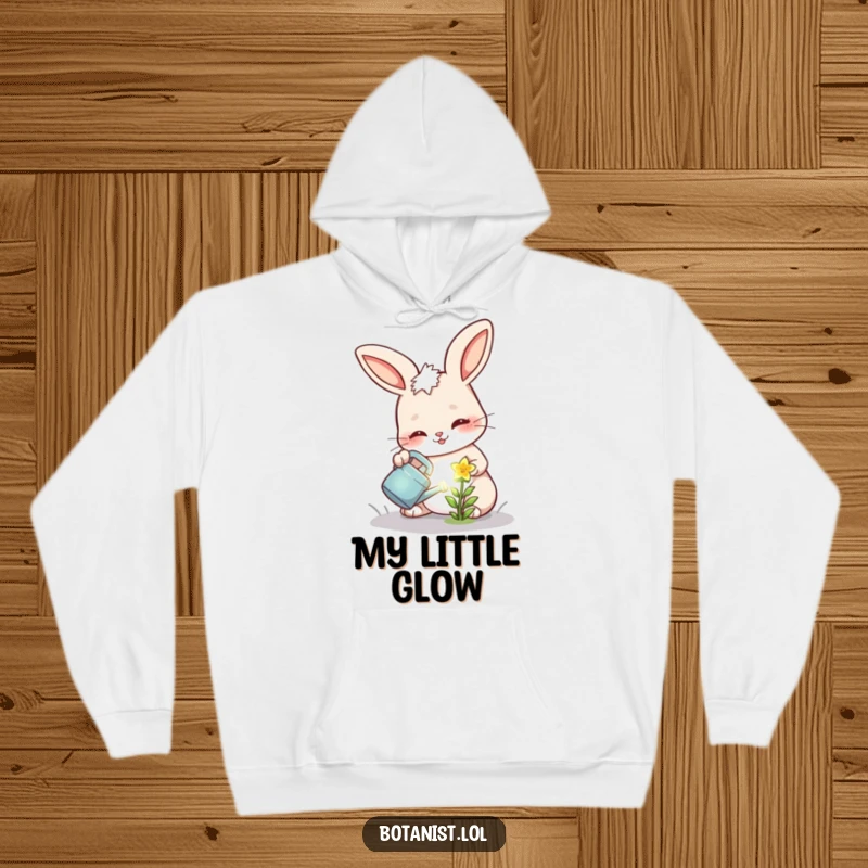 Funny hoodie depicting a cheerful bunny with a determined face, watering a tiny, glowing flower.